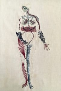 An outline of a naked woman is embroidered on linen in the same bone white colour as the linen. She stands legs together, her right hand covering her groin, her left hand, palm up, extended slightly to her side. She looks to the right. Her body is covered in squiggles, dots, and lines in blues, burgundies, greens and greys. Some of the markings are done in thick stitches, some in thin lines. Her belly is clear of markings. Her face is a mask of green lines, feathery lines cover her shoulders and chest. There is a thick band of intricate burgundy stitching around her waist. Her forearms and hands are covered in thick undulant lines. Her right leg has bands of burgundy along the muscles, with small dots around them. Her inner left leg has a thick line of blue running up it, with thin branches spreading towards her outer leg. 