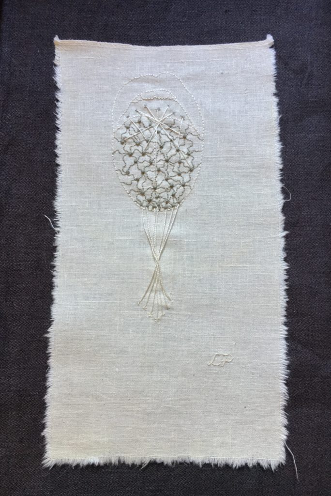An embroidery on bone-coloured linen. There is a pale outline of an open mouth with a tongue sticking out. The tongue is decorated with slightly darker French knots with curved lines between them. There are long threads extending from the tip of the tongue to lower down on the piece where they cross. 