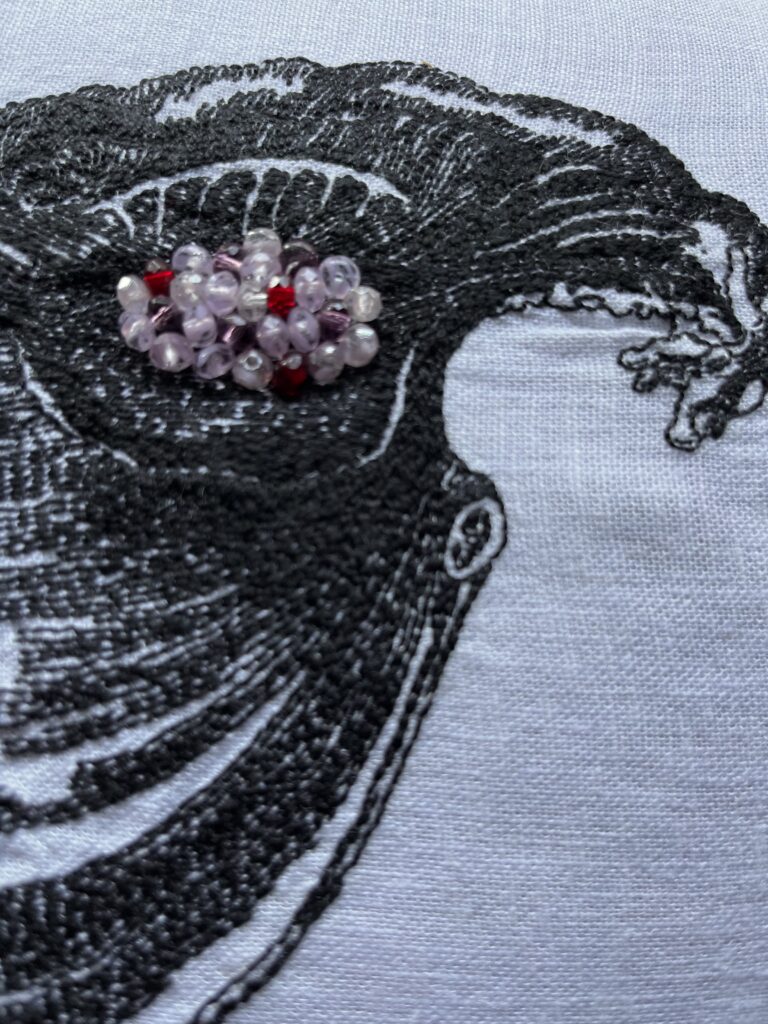 A detail of an embroidery of a Fallopian tube & ovary, in black thread on white linen textured like a woodcut. A cyst on the ovary is in clear, purple, & red beads. The cut edge of the mesometrium can be seen clearly.