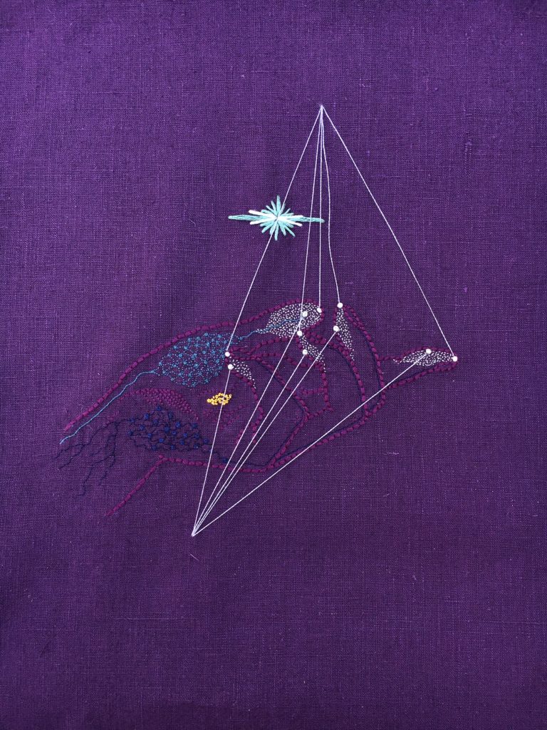 An embroidery on deep purple linen. There is a purple outline of a feminine right hand from the side, palm up, fingers curled slightly inward. There are many tiny white French knots covering the fingertips and light blue, gold, and navy French knots on parts of the palm. There are fine filigree lines connecting many of the French knots and white strands of thread strung from each fingertip to an apex above the hand. There is a starburst floating above the palm in white and light blue. 