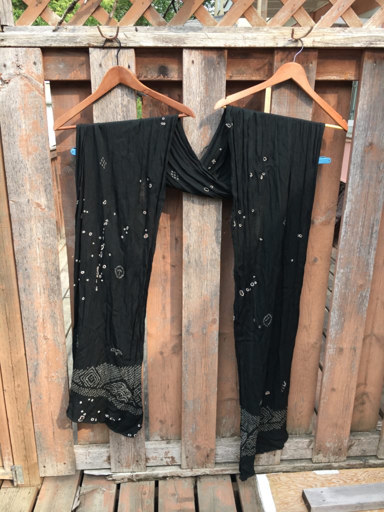 A black scarf/obi with a white design on the ends and many outlined holes.