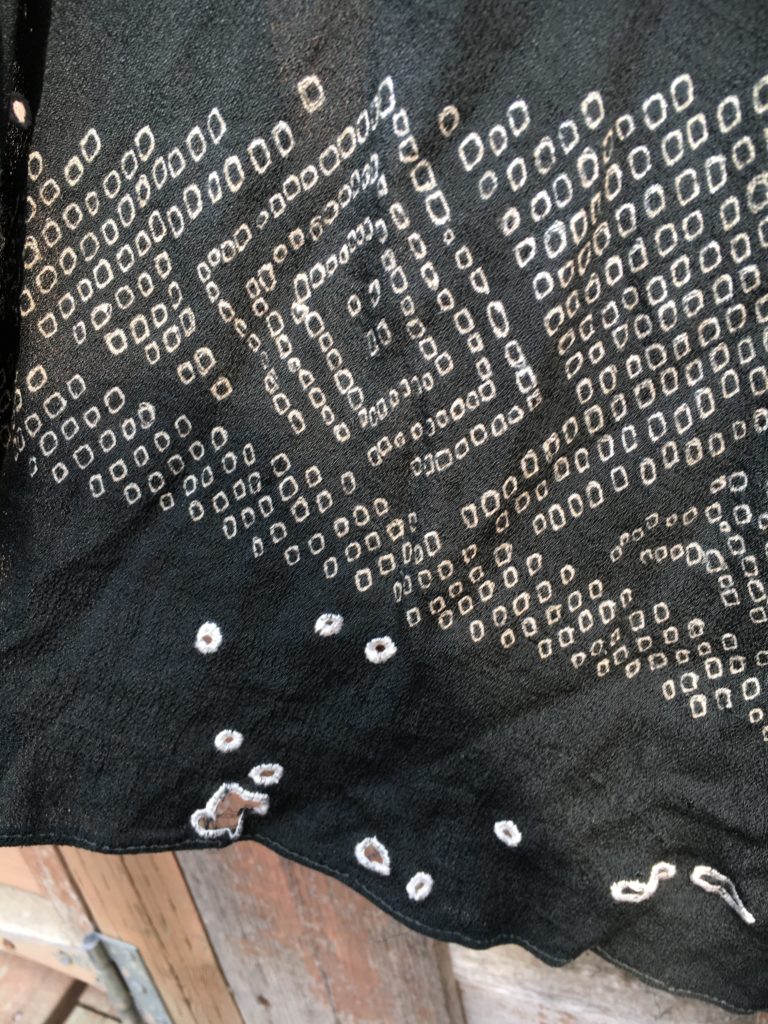 The end of a black scarf/obi showing the original white pattern design plus some buttonholed holes.