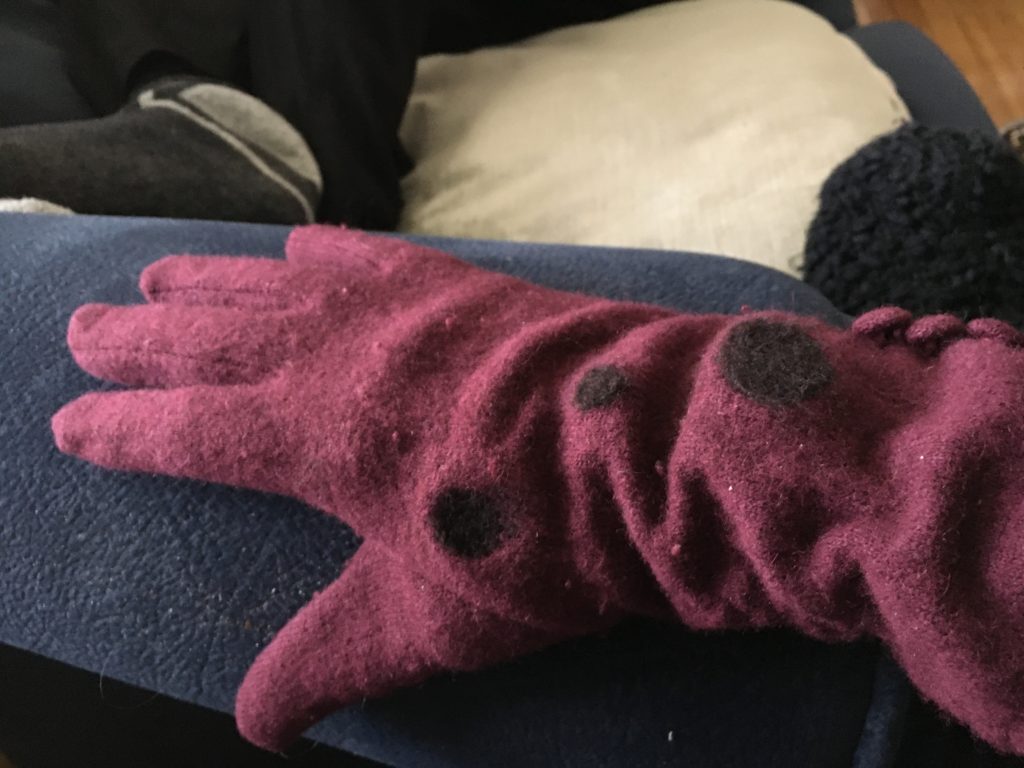 Lia’s hand in a right hand burgundy glove. There are 3 black needle felted dots on the back of the glove.