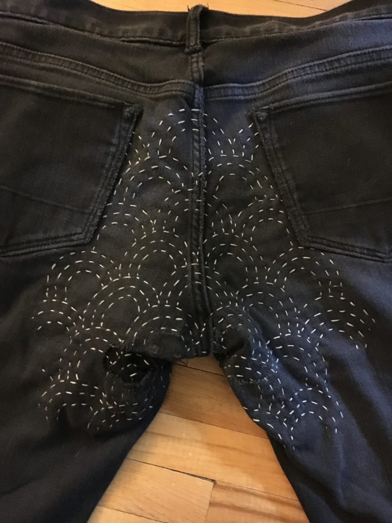 The butt of a pair of black jeans with a Japanese wave pattern on them done in grey sashiko stitching.