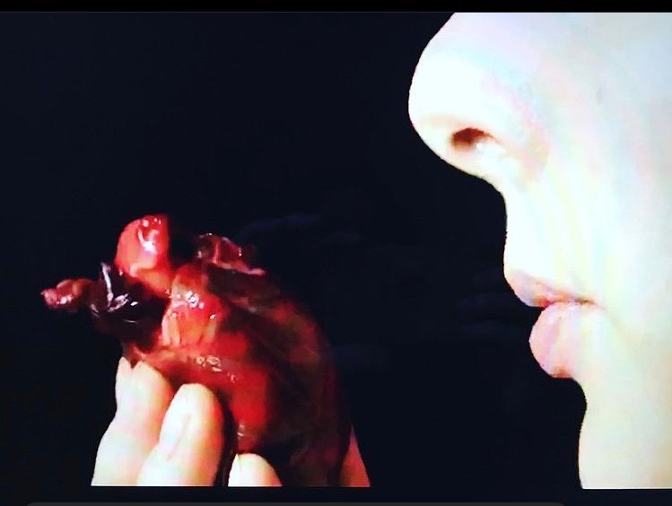A small pig’s heart is held in front of the profile of Lia’s lower face as if she is whispering to it. 
